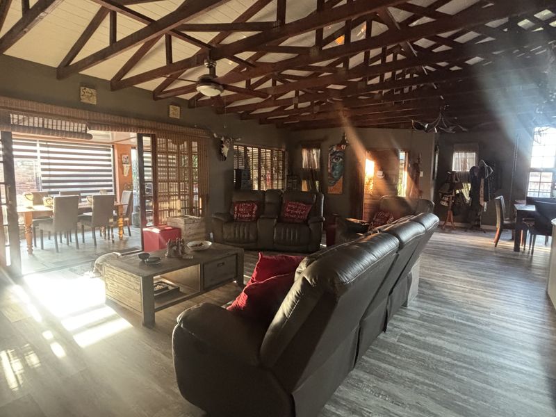 Spacious open-plan living area featuring exposed timber roof trusses, modern laminate flooring, and seamless access to the outdoor patio through large sliding glass doors.