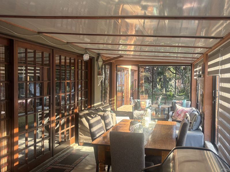A covered patio area featuring a translucent roof, timber-framed glass doors, and roller blinds, providing a bright and versatile outdoor living space.
