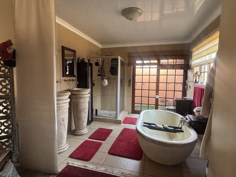 Spacious bathroom featuring a freestanding bathtub, dual pedestal washbasins, a separate shower enclosure, and direct access to an outdoor area through french doors.