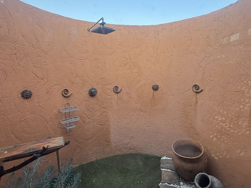 An outdoor shower area featuring a curved wall with a textured finish and a fixed shower head.