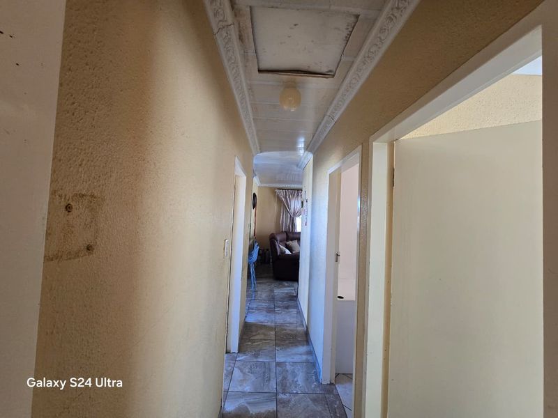 A narrow hallway featuring tiled flooring and decorative ceiling cornicing, showing signs of wear and requiring cosmetic updates.