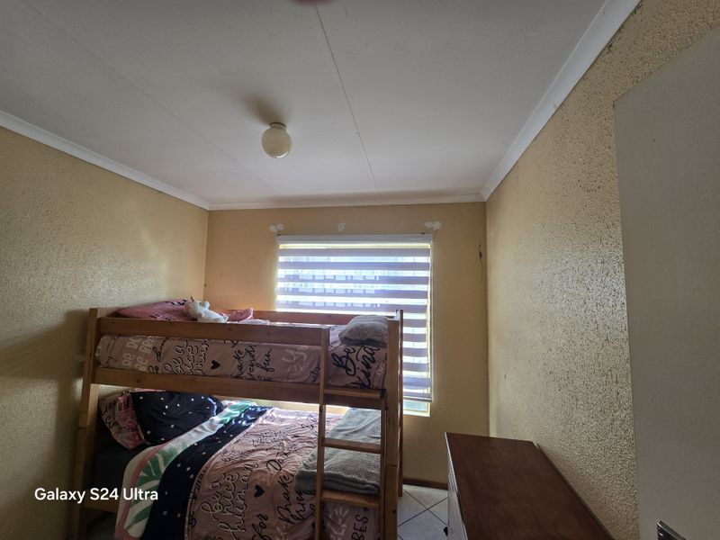 A bedroom featuring textured walls, tiled flooring, and a window with a roller blind. The room shows signs of wear and requires cosmetic attention.