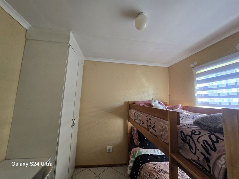 A bedroom featuring a built-in wardrobe, tiled flooring, and a window with a roller blind. The room requires cosmetic updates to the wall finishes.