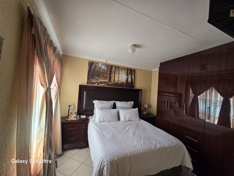 A functional bedroom featuring built-in dark wood cupboards and tiled flooring, offering a comfortable and practical living space.
