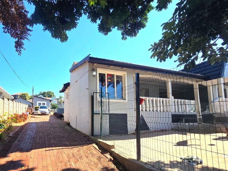 Front exterior view of the house featuring a brick driveway, wire mesh fencing, and a covered patio area with a concrete balustrade.