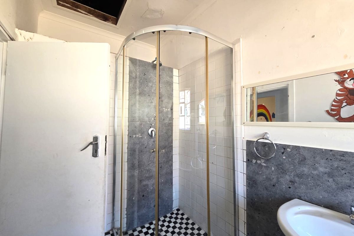 A dated bathroom featuring a curved shower enclosure, wall-mounted basin, and checkerboard floor tiles, requiring cosmetic updates and ceiling repairs.