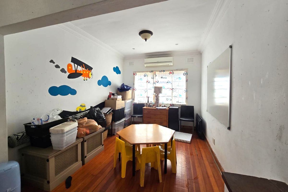 A bedroom featuring hardwood flooring, a split-system air conditioner, and cornice detailing, currently used as a play area with visible wall scuffs.