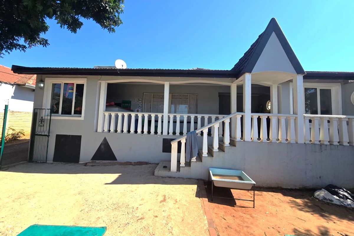 Rear view of the house featuring a covered patio with a balustrade, staircase, and tiled roof structure.