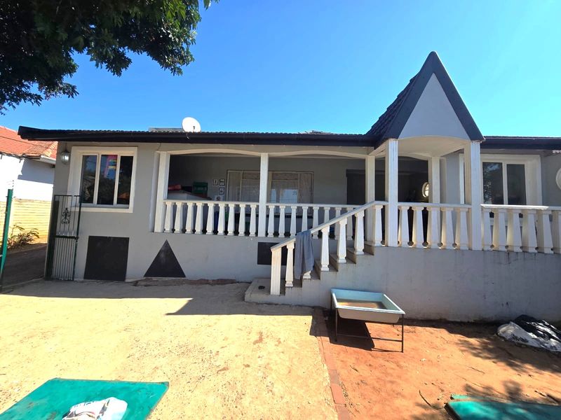 Rear view of the house featuring a covered patio with a balustrade, staircase, and tiled roof structure.