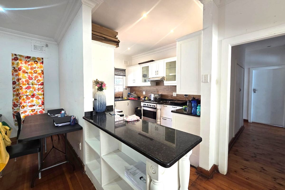 A functional kitchen featuring white cabinetry, dark granite countertops, a stainless steel stove, and warm timber flooring, with an open-plan layout.