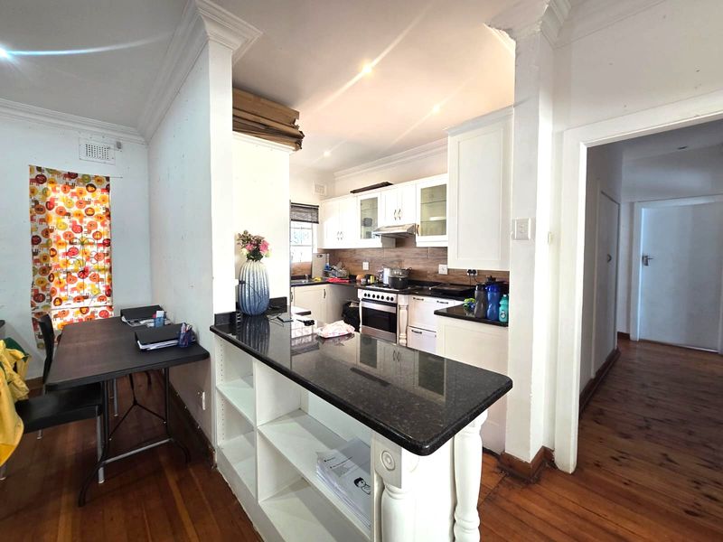 A functional kitchen featuring white cabinetry, dark granite countertops, a stainless steel stove, and warm timber flooring, with an open-plan layout.