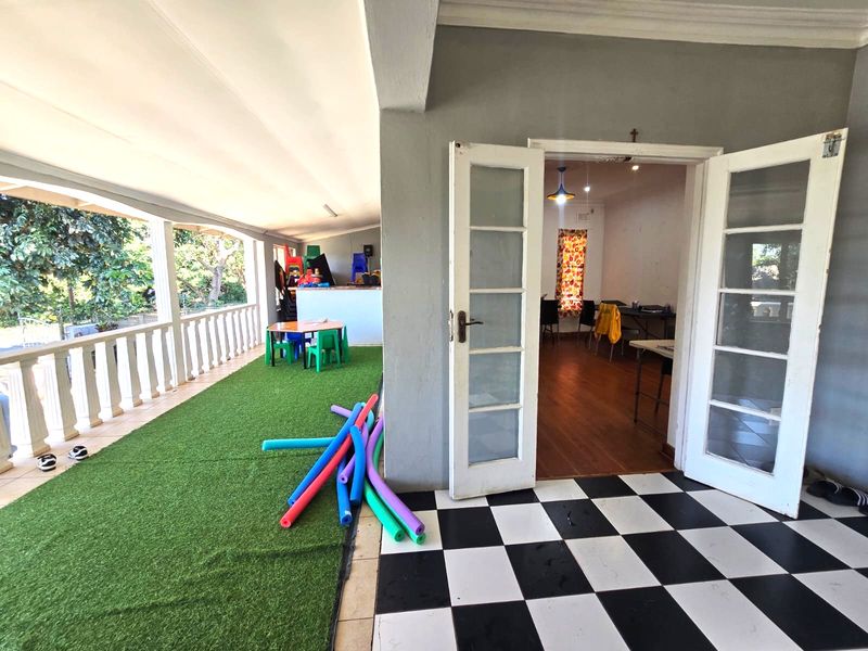 Covered patio area featuring artificial grass, a classic checkered tile entrance, and double french doors leading into the interior living space.
