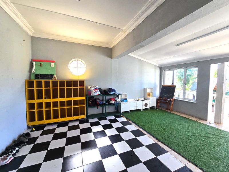 A multi-purpose utility space featuring checkered tile flooring, a circular window, and crown molding, currently utilized as a play area.
