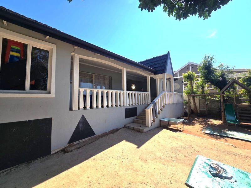 Rear view of the house featuring a covered patio with a balustrade, concrete stairs, and a spacious backyard area.