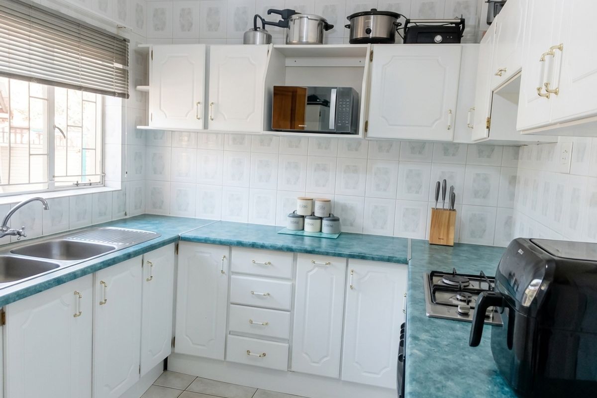 A functional kitchen featuring white cabinetry, teal laminate countertops, a double bowl sink, and a built-in gas hob with tiled wall finishes.