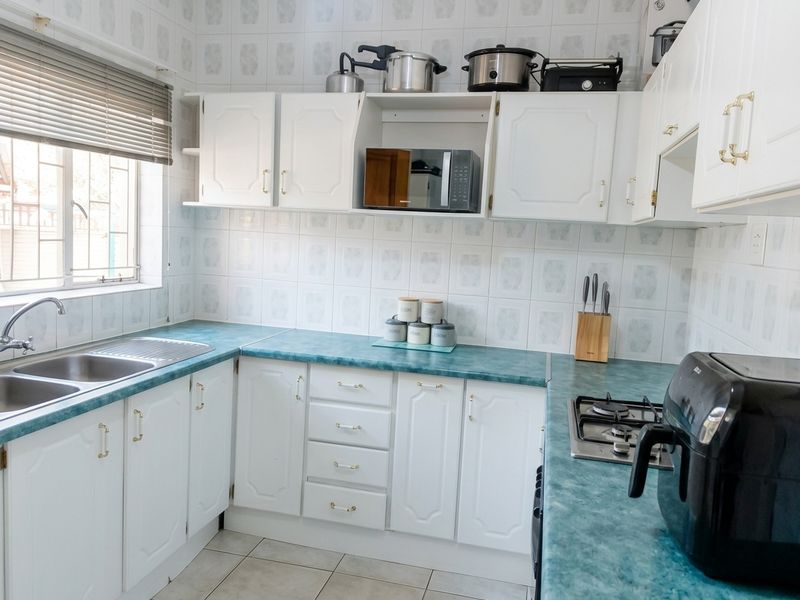 A functional kitchen featuring white cabinetry, teal laminate countertops, a double bowl sink, and a built-in gas hob with tiled wall finishes.