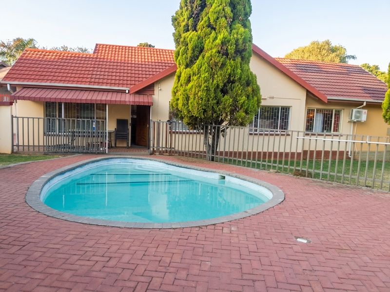 Rear exterior view featuring a swimming pool, paved patio area, and a single-story house with a tiled roof and security fencing.