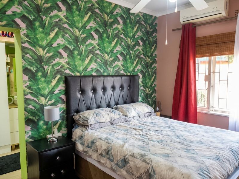 A bedroom featuring a bold tropical-patterned accent wall, a ceiling fan, and a wall-mounted split-system air conditioner.