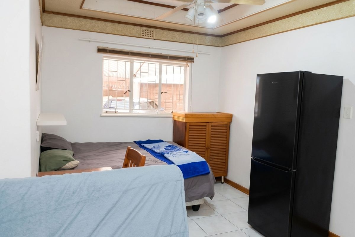 A bedroom featuring tiled flooring, a ceiling fan, and a window with security bars, offering a functional space with dated ceiling detailing.