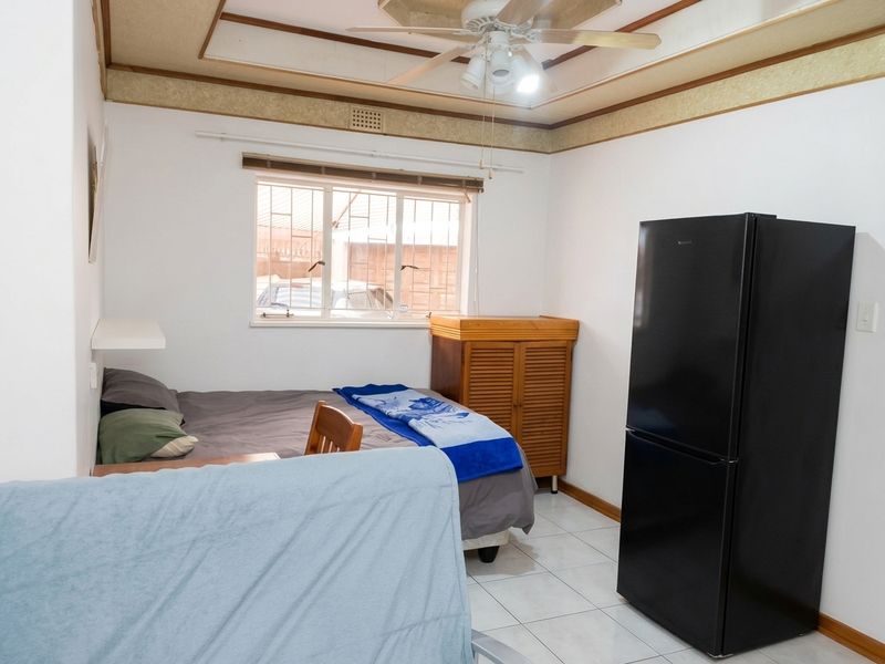 A bedroom featuring tiled flooring, a ceiling fan, and a window with security bars, offering a functional space with dated ceiling detailing.