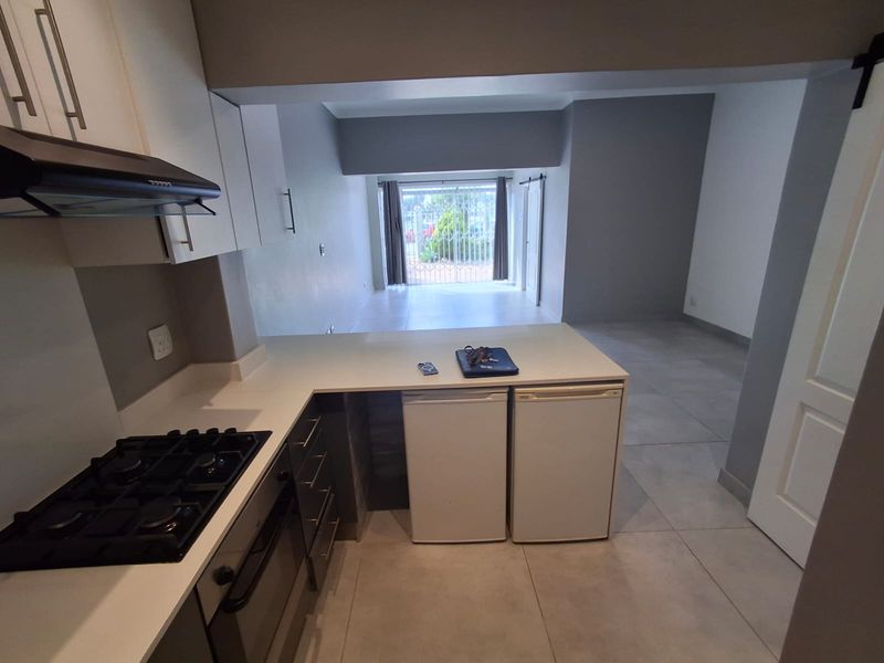 Open-plan kitchen and living area featuring modern cabinetry, gas hob, built-in oven, and neutral tiled flooring leading to a secure exterior entrance.