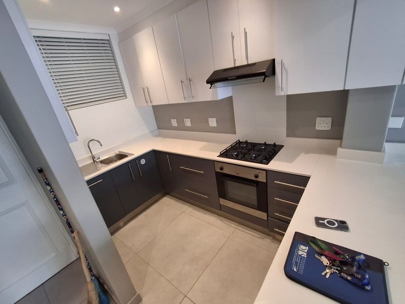 Modern kitchen featuring dark lower cabinetry, white upper cabinets, stone countertops, a gas hob, built-in oven, and tiled flooring.