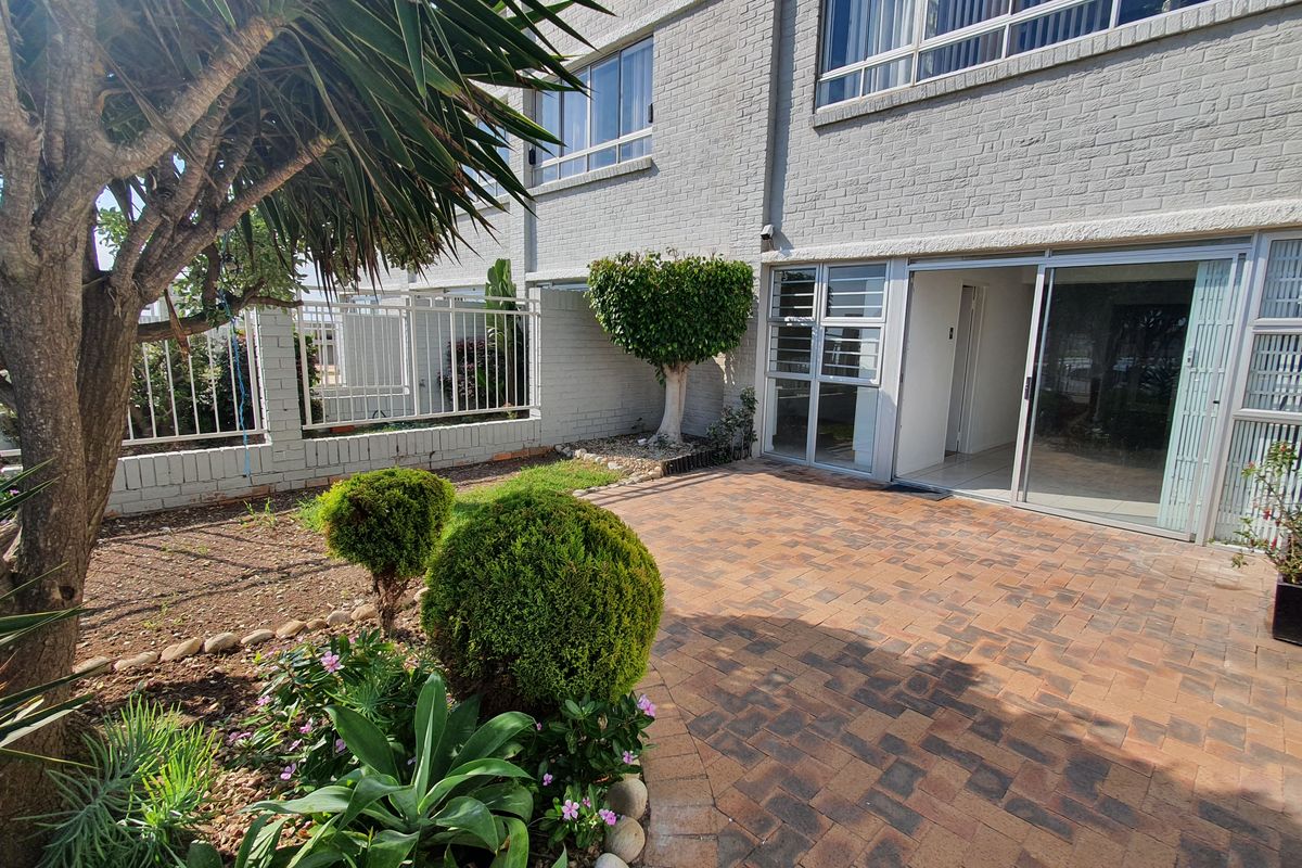 A private rear patio area featuring brick paving, sliding glass door access, and established garden landscaping against a painted brick apartment facade.