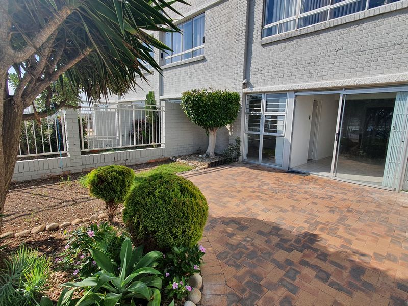 A private rear patio area featuring brick paving, sliding glass door access, and established garden landscaping against a painted brick apartment facade.