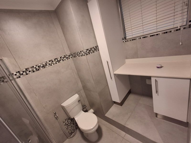 A modern bathroom featuring grey wall and floor tiles, a built-in vanity unit, a shower enclosure, and a toilet.