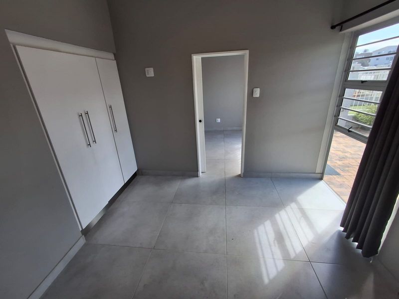 A clean, empty bedroom featuring modern large-format floor tiles, built-in cupboards, and direct access to an outdoor patio area through a windowed door.