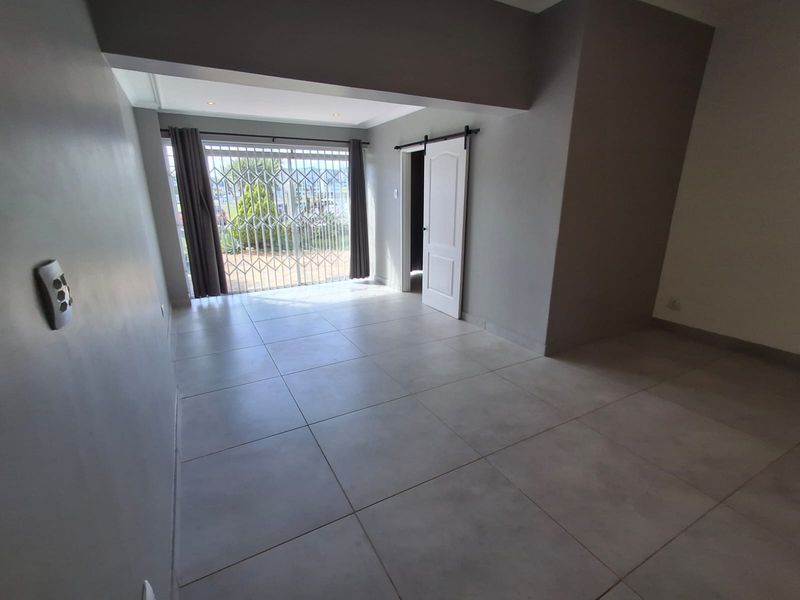 A bright, empty living area featuring neutral tiled flooring, recessed lighting, and a modern sliding barn door leading to an adjacent space.