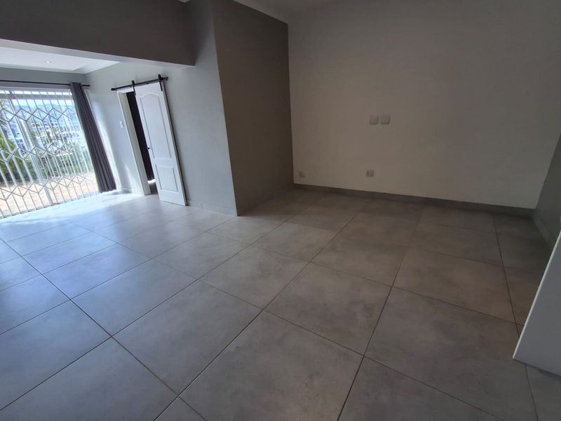 A spacious, empty living area featuring large format grey floor tiles, a sliding door with security gate, and a modern barn-style door.
