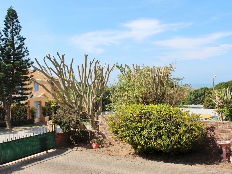 A view of the front garden area featuring a paved driveway, brick boundary wall, and established trees and shrubs.