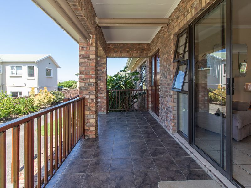 A covered patio featuring brick pillars, tiled flooring, and a timber balustrade, providing seamless access to the interior living space through sliding glass doors.
