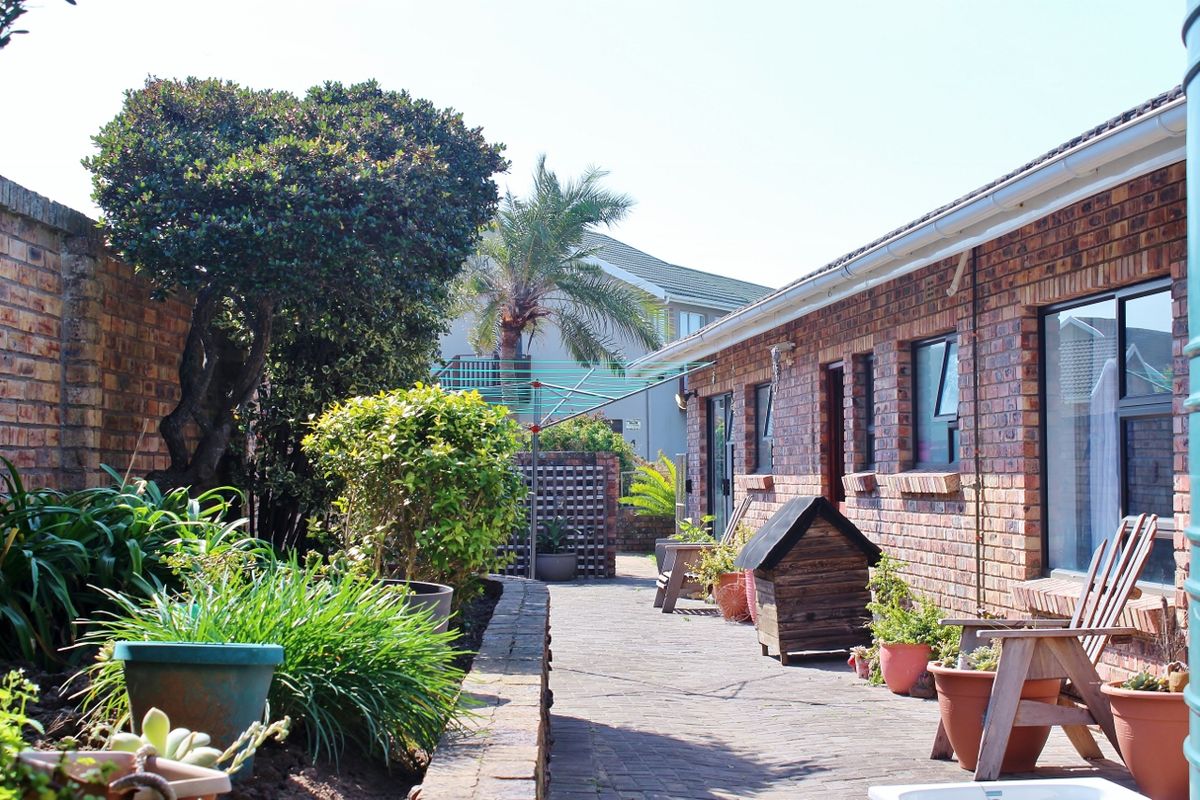 A private rear courtyard featuring face brick walls, paved flooring, and established garden beds, providing a low-maintenance outdoor living space.