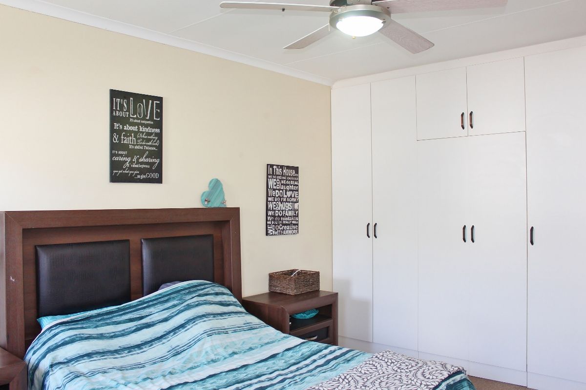 A bedroom featuring white built-in cupboards and a ceiling fan, providing functional storage and climate control.