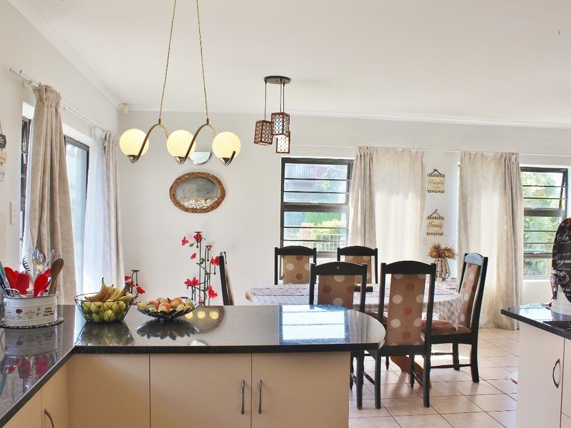 Open plan kitchen and dining area featuring granite countertops, tiled flooring, and ample natural light through louver windows.