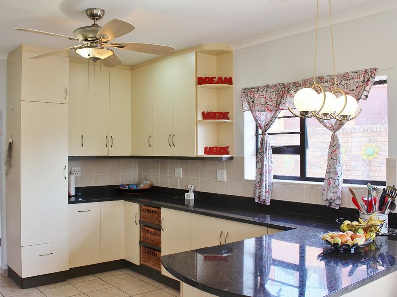 A functional kitchen featuring granite countertops, ample built-in cabinetry, tiled flooring, and a ceiling fan, with a window overlooking the exterior.