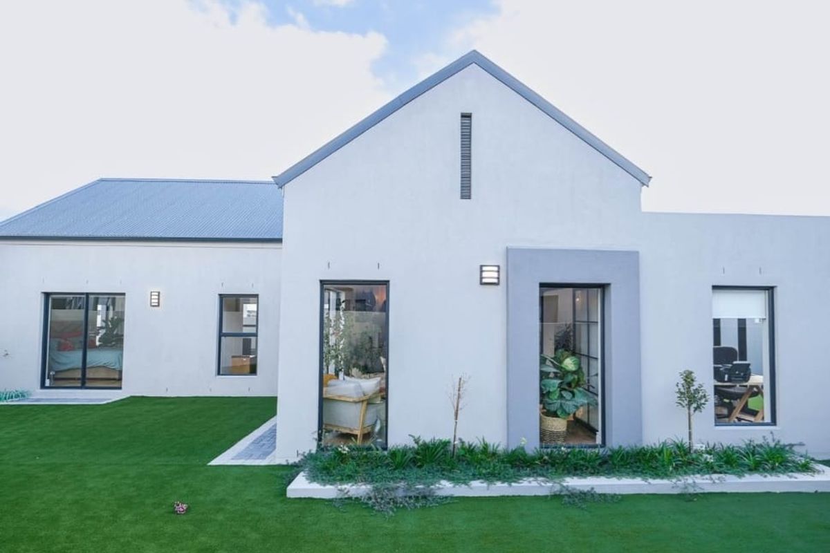 A modern rear elevation of a house featuring clean white rendered walls, dark aluminium window frames, a metal roof, and a well-maintained artificial lawn.