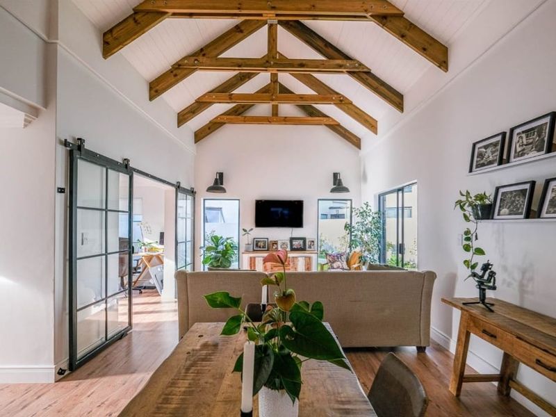 Spacious open-plan living and dining area featuring a striking vaulted ceiling with exposed timber trusses, hardwood flooring, and elegant sliding glass doors.