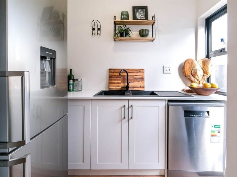 A modern, well-maintained scullery featuring white cabinetry, stone countertops, a black sink with matching tap, and integrated dishwasher.