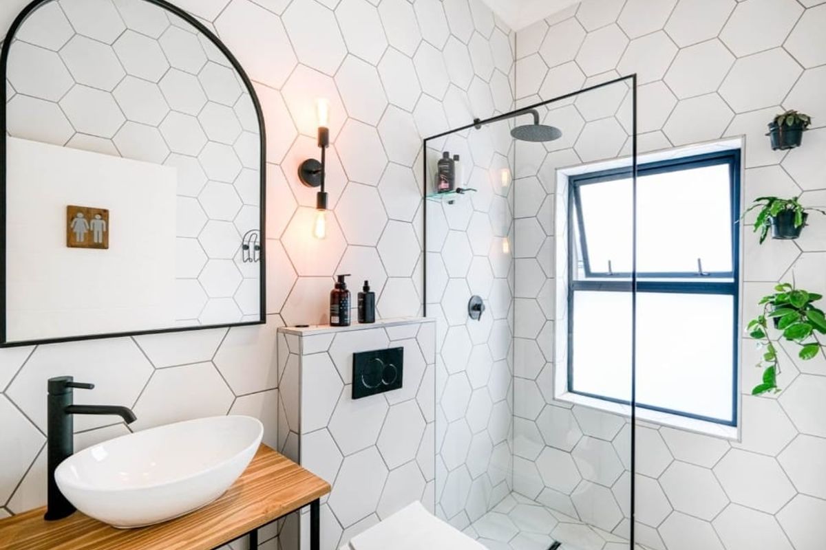 Modern bathroom featuring hexagonal wall tiles, a walk-in shower with black frame, wall-mounted toilet, and a stylish vessel sink on a wooden vanity.