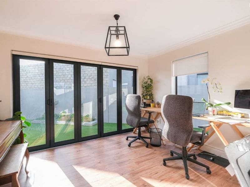 Bright home office featuring modern black-framed bi-fold doors that open to the garden, laminate flooring, and contemporary lighting.