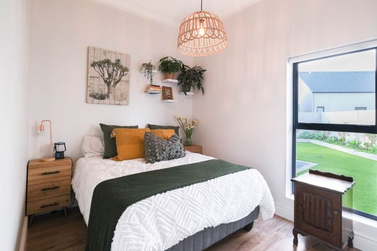 A well-maintained bedroom featuring laminate flooring, modern aluminium window frames, and a decorative pendant light fixture with views of the garden.
