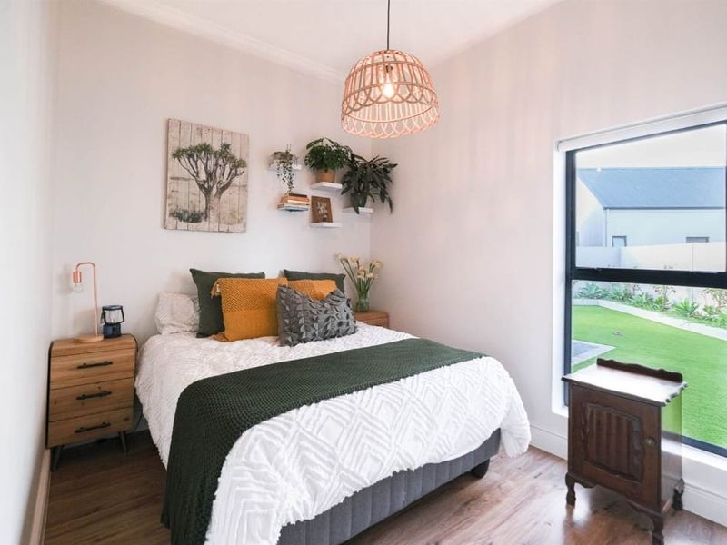 A well-maintained bedroom featuring laminate flooring, modern aluminium window frames, and a decorative pendant light fixture with views of the garden.