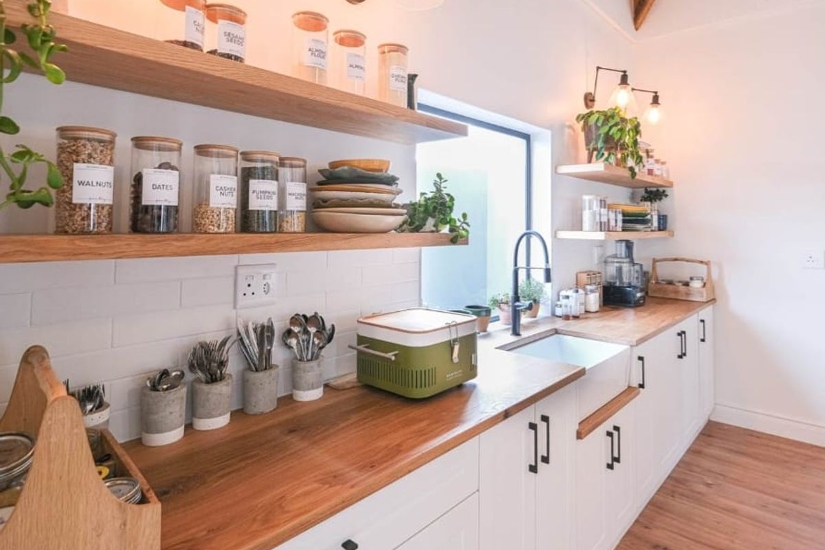 Modern kitchen featuring white shaker cabinetry, warm wooden countertops, a classic butler sink, subway tile backsplash, and exposed timber ceiling beams.
