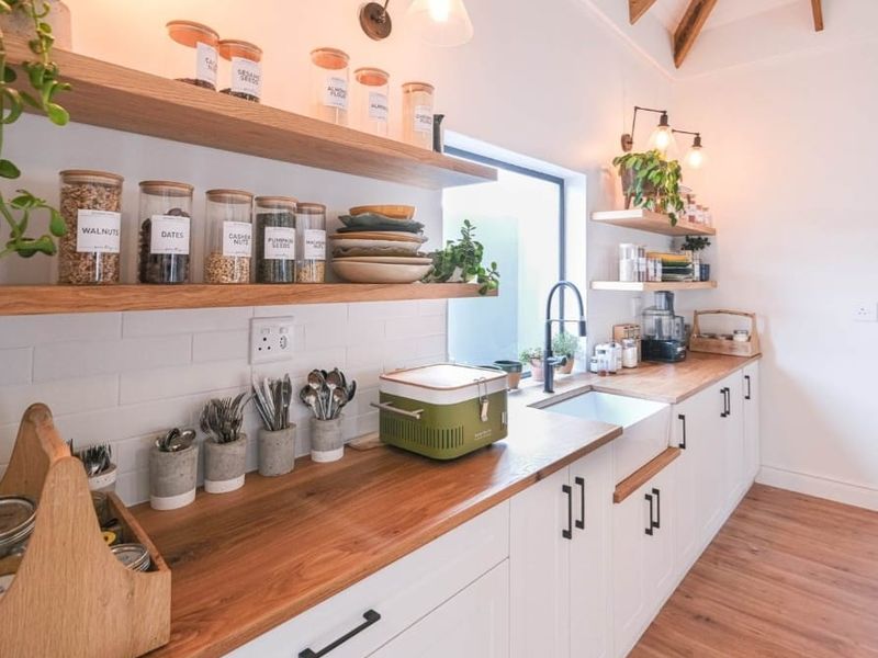 Modern kitchen featuring white shaker cabinetry, warm wooden countertops, a classic butler sink, subway tile backsplash, and exposed timber ceiling beams.