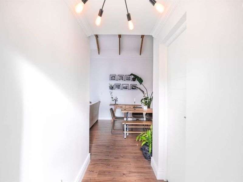 A bright hallway featuring laminate flooring and exposed timber ceiling beams, leading into an open-plan living and dining area.