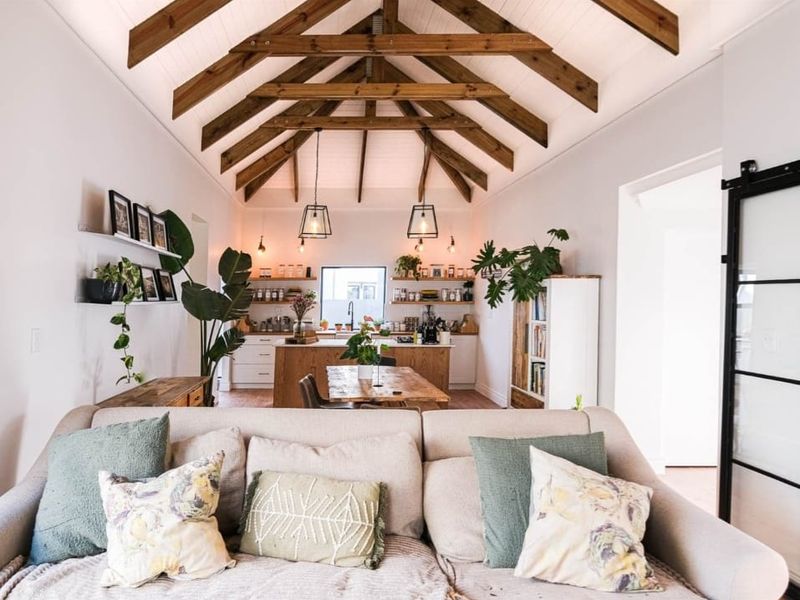 An open-plan living and kitchen area featuring a high vaulted ceiling with exposed timber trusses, a central kitchen island, and modern finishes.