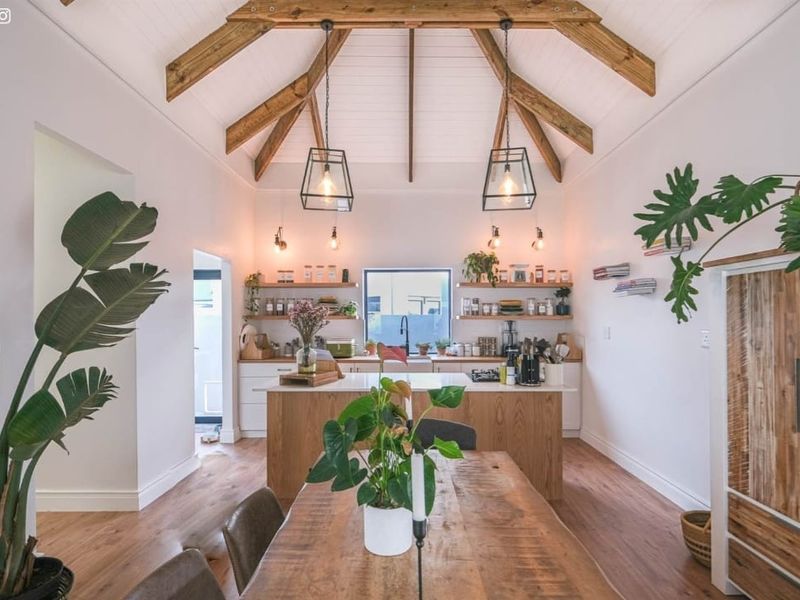 Open-plan kitchen and dining area featuring high vaulted ceilings with exposed timber trusses, modern cabinetry, and warm timber flooring.